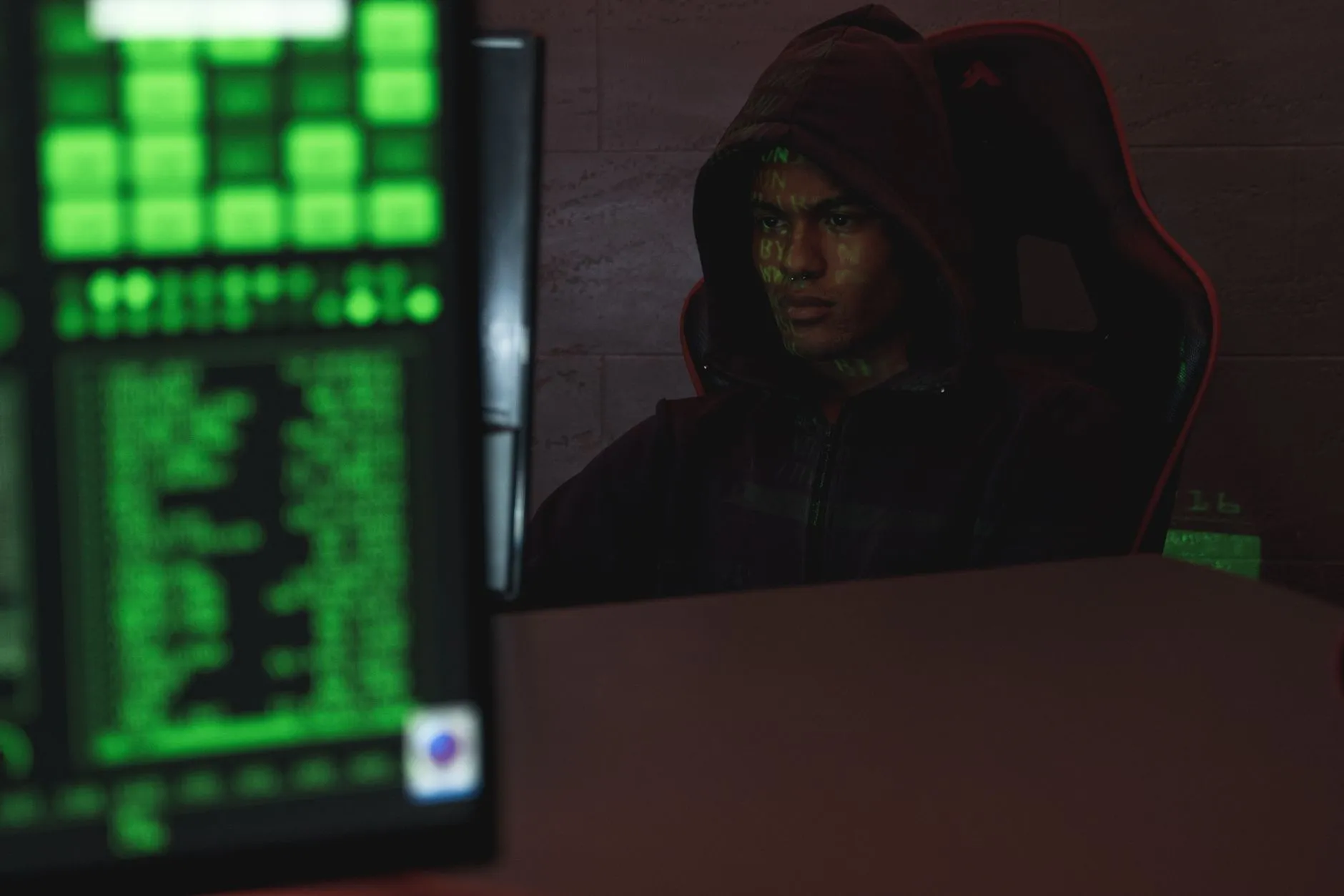 A hooded figure at a keyboard with code on screen, representing a governance exploit of a DeFi protocol.
