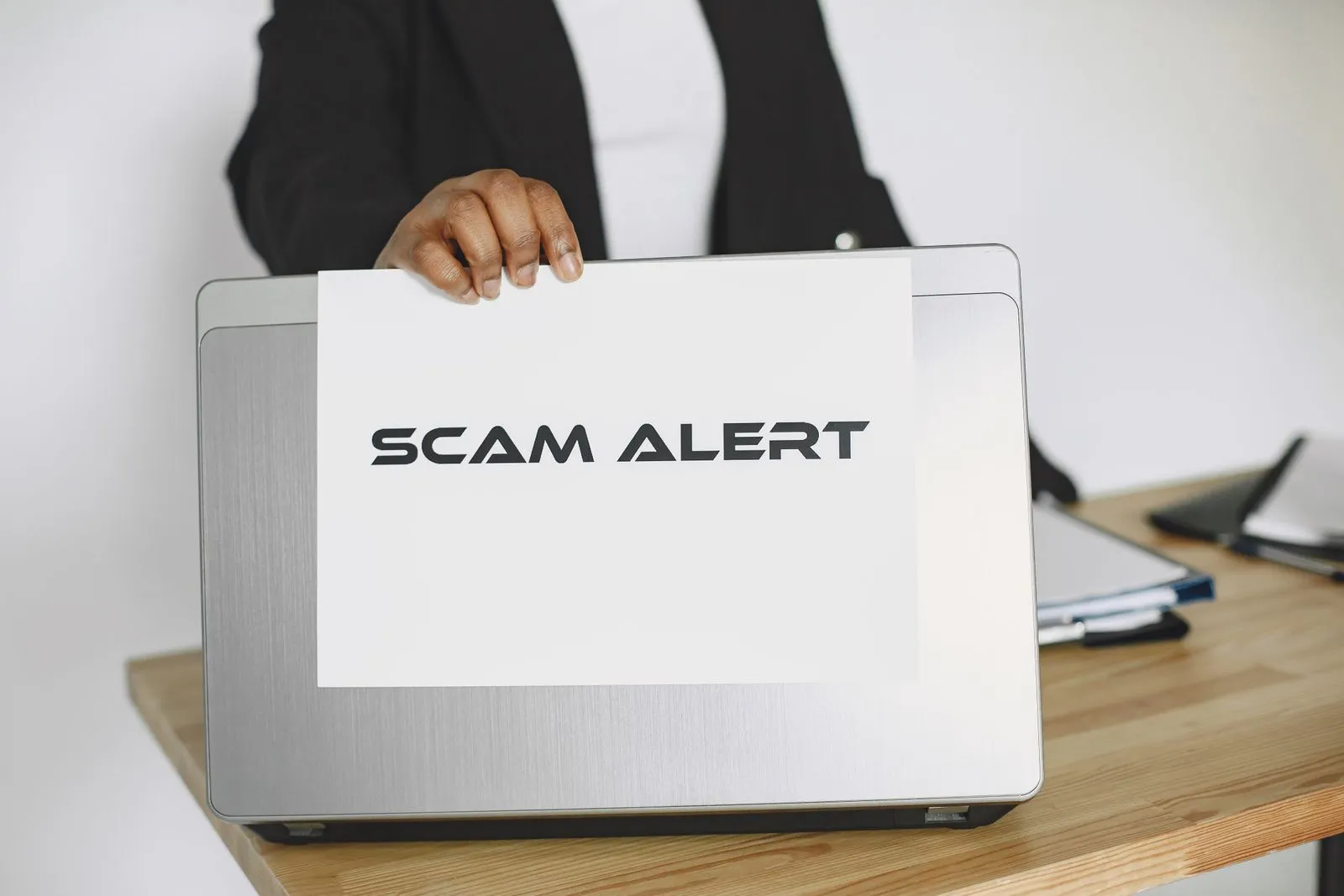 A person holds a scam alert sign beside an open laptop, illustrating a phishing campaign.